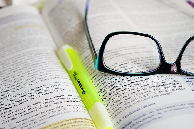 Glasses and pen leaned on a dictionary