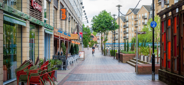 A wide pavement with restaurants to the left and a river to the right.