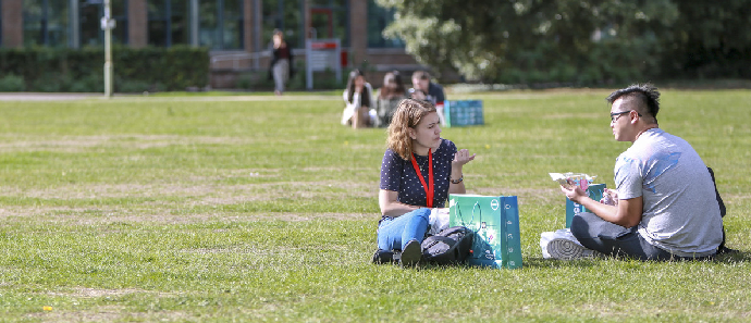 Two students sit and talk on the grass.