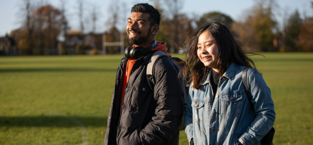 Two students walking on a field laughing with each other