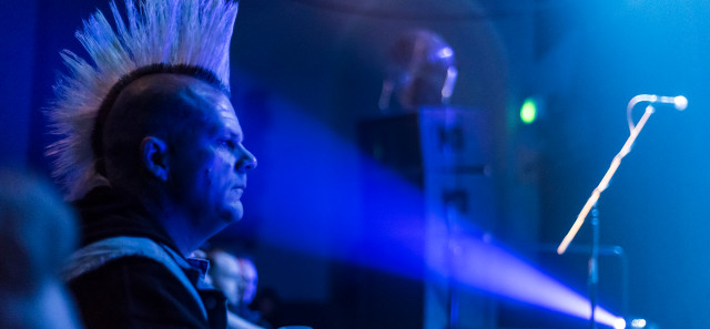 Man with mohawk on stage lit by spotlight
